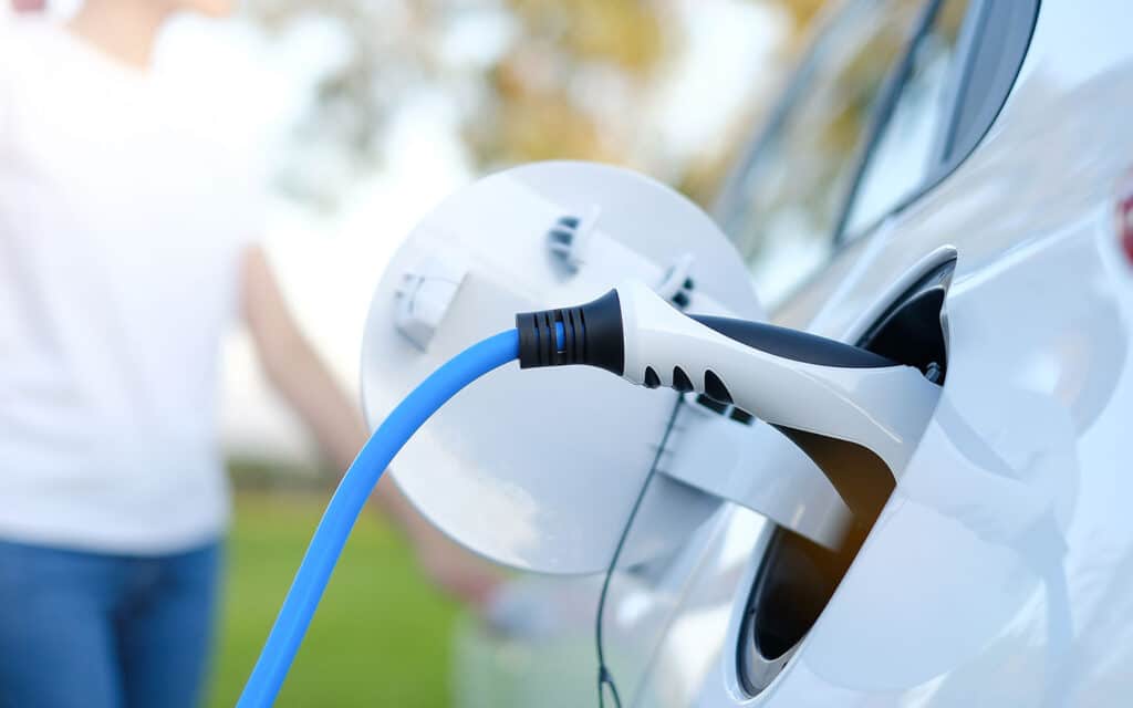 Recharge de voiture électrique avec câble et pistolet Voiture électrique blanche en cours de recharge avec un câble bleu et un pistolet de charge noir et blanc.